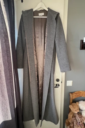 Exklusiv kappa grå - Grå lång kappa av väldigt fin kvalité. Kappan har huva och är lång, så lång att den nästan går ner till fötterna (beroende på hur lång man är såklart).   