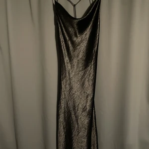 Svart långklänning  - Svart långklänningi svart blankt material med snörning i ryggen från Gina  Endast använd 1 gång 