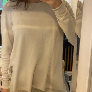 Stickad tröja  - Säljer denna stickade tröja från Vila, med rosetter och slitsar på sidorna. Fint skick, endast använd ett fåtal gånger. 