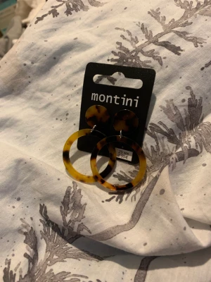 Örhängen - Helt nya Montini örhängen. Säljes för 20kr. Köparen står för frakten. Kan skicka spårbart och icke spårbart. Kan mötas upp i Örkelljunga men även på annan plats. (Om du beställer flera saker kan ja skicka de i ett packet)