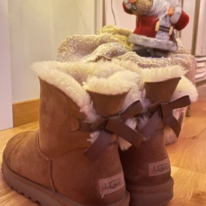 Ljusbruna Uggs - PRIS KAN DISKUTERAS!  Ljusbruna uggs med rosett! Så söta! Men dom kommer inte till användning mer tyvärr. Storlek 41 funkar för 40 också!  Nypris 2150kr sänkt på grund av att deär använda:)  Återkommer om frakt