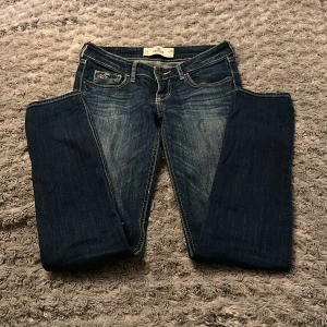 Jeans från Hillstierna. - Lågmidjade. Strl 26/31. Trasig söm nedanför knät, ej hål.