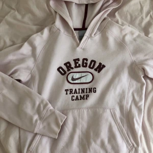 nike hoddie  - En ljus rosa Nike hoddie med vinröd text och logga över bröstet. Skicket är inte toppen; den är nopprig och har någon fläck (bild 3). Storlek Xl för age 13/15 så mer typ S (men lång i ärmarna). Skriv för fler bilder eller vid frågor!