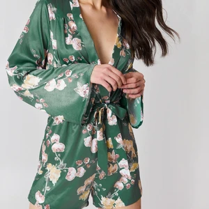 Satin Playsuit från NA-KD - En super fin deep v-neck playsuit från NA-KD. Perfekt nu till sommaren! Den har långa utsvängda armar och är extremt skön i tyget som är i satin. Storlek 36. Använd endast ett fåtal gånger. Måste sälja den då den är för liten för mig. 