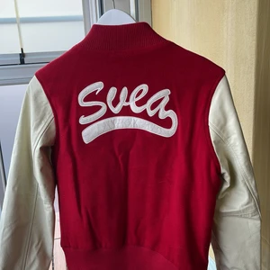 Svea baseballjacka  - Baseballjacka från Svea, oversized i strl M. Fakeskinn på armarna i en off white och röd på mittenpartiet.  50% Ull, 50% viskos.  I mycket bra skick. 
