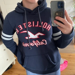 Hollister blå huvtröja/hoodie - Mörkblå Hollister hoodie med vita och röda detaljer, väldigt mjuk! Väl använda men ändå bra skick, passar allt från xxs-l 😊  Pris kan diskuteras vid snabb affär, frakt betalas av köparen.  Skriv gärna om ni har frågor eller vill ha fler bilder!💕