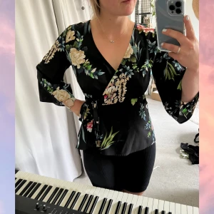 Blommig Sommarblus - Omlottblus med vidare ärmar och med fint fall under bysten. Sparsamt använd och stretchigt material. Strl: XS, men kan absolut fungera upp till M/L tack vare omlott + stretch. OBS! Cirkapris på frakten, kostnad kan tillkomma. 