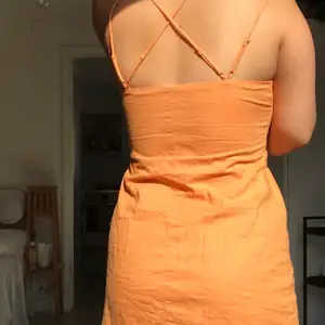 En orange linneklänning från H&M. Korsade band i ryggen, dragkedja på sidan, halvkort klänning.  Har tyvärr tagit bort lappen i ryggen så vet inte storleken men skulle gissa  på M.  !Behöver strykas !(har inget strykjärn)👀   🌸Frakt tillkommer🌸 