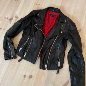 Skinnjacka  - Skinnjacka från Rock’n Blue (Madde in Sweden). Har varit mycket omtyckt, ompysslad och använd. Passar som en 36a eller 38a. Köpt för ca. 2000kr.