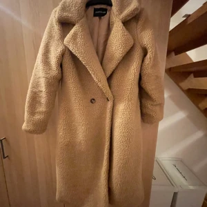 Lång teddy kappa - Hej, jag säljer en ’teddy’ kappa som jag tror är ifrån madlady, använd 1 gång då den inte riktigt var min stil. Storlek 36 men passar nog några storlekar större. 