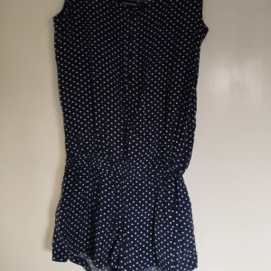 Jumpsuit S - En prickig och härlig jumpsuit i marinblått, har fyra knappar framtill också. Är i väldigt bra skick då den inte är använd många gånger.