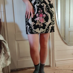 Mönstrad kjol - En kjol av ett styvt material med fint mönster.   Midjemått: 74 cm. Längd: 40 cm