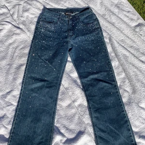 Coola jeans med rhinestones - Sjukt snygga jeans som inte kommer till användning! Köpta på beyond retro och insydda i midjan men går lätt att ta upp✨ Midwaist och lite utsvängda/bootcut ben. Galet fina i solen!!🤩 Kan skicka mått om så önskas. Köpare står för frakt