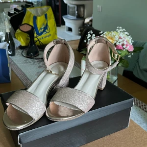 Guld glittriga klackskor  - sandalett klacksko i snyggt glittrigt material med blockklack och en öppen rundad tå. Reglerbar vristrem och en klackhöjd på 5,5 cm.  Endast använda en kväll så fortfarande i mycket gott skick!  Köpare står för frakt 