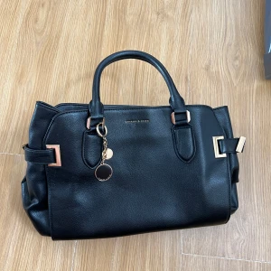 Märkes handväska - Märkesväska charles&keith. Den är i bra skick. Svart med gulddetaljer. Väskan har fickor och är medelstor. 
