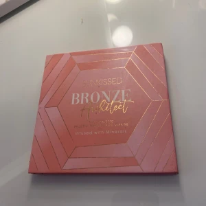 Sunkissed Bronze Highlight Palette - Säljer en superfin Sunkissed Bronze Highlight Palette. Den innehåller fyra olika nyanser: en rosa blush , två bruna bronzers och en gyllene highlighter. Perfekt för att skapa en solkysst look med lite extra glow. Paletten är infuserad med mineraler för en mjuk och jämn applicering. Den kommer i en snygg rosa förpackning med guldiga detaljer.
