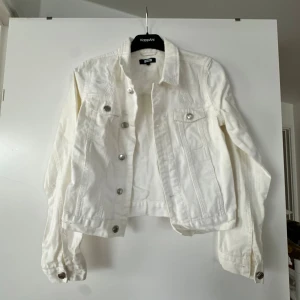Vit jeans jacka  - Oversized jeansjacka med vintage look. Jackan är vit och har knäppning fram. Den har nedhasad axel, bröstfickor med lock, krage, reglerbar slejf med knapp i sidorna och lång ärm med knapp och manschett.