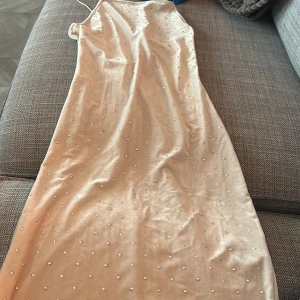 Champagnefärgad långklänning med pärlor - Säljer en elegant champagnefärgad långklänning med pärlor. Klänningen är ärmlös och har en öppen rygg, vilket gör den perfekt för festliga tillfällen. Materialet känns lyxigt och klänningen har en tight passform som framhäver figuren. Perfekt för sommarens alla fester! 🌟