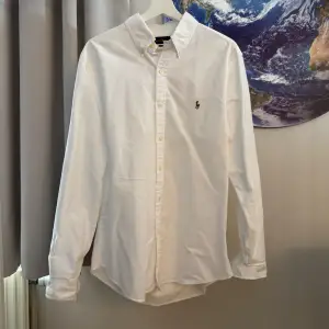 Säljer en snygg vit skjorta från Ralph Lauren i storlek L. Skjortan är slim fit och har långa ärmar. Den är gjord av bomull och har knappar längs framsidan. Perfekt för både fest och vardag!