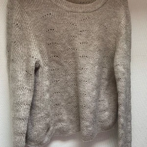 Beige stickad tröja från ONLY - En beige stickad tröja från ONLY med ett diskret mönster. Tröjan har långa ärmar och en rund halsringning.