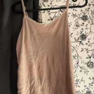 Beige ribbad linnetopp - Säljer en snygg beige ribbad linnetopp. Den är ärmlös med smala axelband och har en enkel men stilren design. Perfekt för sommaren eller som ett basplagg i garderoben. Toppen är i bra skick.