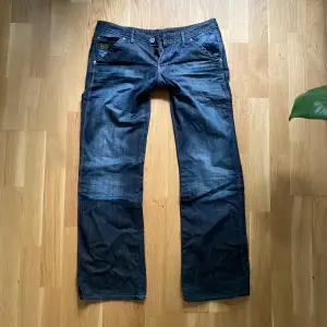 Säljer ett par snygga mörkblå jeans från G-Star RAW i storlek 30/32. Jeansen har en straight fit och är tillverkade i slitstarkt denim. De har klassiska fem fickor och knappar i midjan. Perfekta för både vardag och fest!