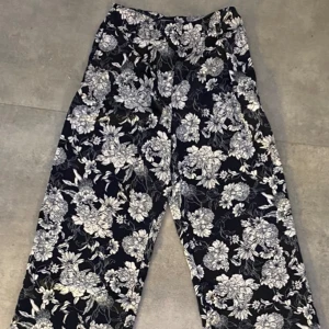 Tygbyxor- black/off-white - En elegant byxa med en blommig mönster som är i nytt skick och använd endast ett par gånger. Den har en sidenlen känsla på både insidan som utsidan. Ny utan prislapp.