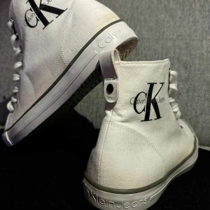 Calvin Klein sneakers - Snygga vita tygskor från Calvin Klein.  Storlek 40 US 7  Dom är sparsamt använda men tyvärr dragit på sig lite färgskiftning, men fortfarande i väldigt fint skick.   Se bilder ☺️