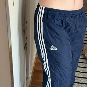 Mörkblåa adidas byxor som jag köpt secondhand.  - Snygga baggy Mörkblåa adidas byxor! Perfekt för att träna i eller dansa i. Dem har dragkedjor vid anklarna om man vill ha en mer flared look. Finns en liten missfärgning på ena knät 