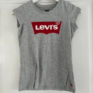 Grå figursydd t-shirt med Levistryck. Fint skick storlek 140. 
