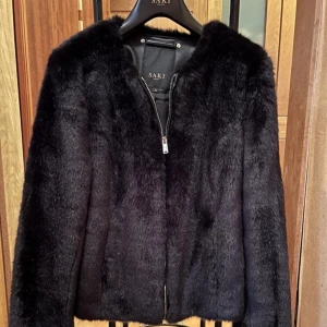Vår pälsjacka Saki  - Säljer min pälsjacka (faux fur) från Saki i svart. Inköpt på Johnells för några år sen. Stängs med silvrig dragkedja. Använd enstaka gånger så där av i väldigt fint skick.  Medföljer även en galge om så vill från Saki.  Kan skickas eller mötas upp. 