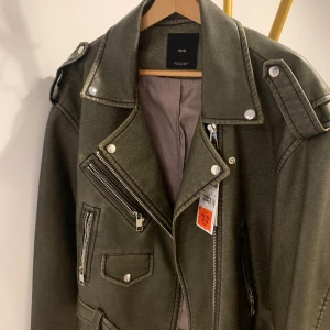 Fake skinnjacka - Sprillans ny skinnjacka i grågrön trendig färg! Helt oanvänt och köpt på MANGO för 599. Säljer för 450kr. Storlek S men passar även M.