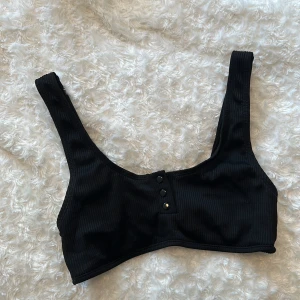 Bikinitopp - Svart topp i machester-liknande tyg. Man kan knäppa eller knäppa upp knapparna hur man vill. Mycket sparsamt använd