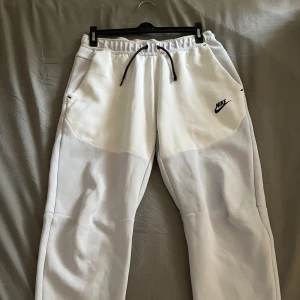 Nike byxor - Bekväma Nike Tech byxor i vit och ljusblå nyans. Byxornas skick är väldigt bra bortsett från att byxornas snören är skadade. Rekommenderas inför sommaren☀️☀️