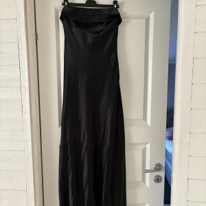 Svart satinklänning - Svart lång satin klänning, aldrig använd lappen kvar. Säljer då den tyvärr är lite lång på mig som är 163 cm. Den har resår på ryggen vilket gör att den sitter uppe ordentligt! Perfekt till bal eller fest😍