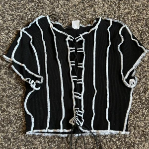 Svart vit tröja med tråd - Nästan helt oanvänd. Svart magtröja med vita trådar som sticker ut mer, har svarta snören i mitten så man kan justera hur öppen tröja ska va