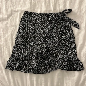 kjol - svart kjol med vita blommor på, har volang i nederkanten, samt en detalj som följer hela vägen upp till knytningen. jättefin till sommaren och har inga defekter🌸