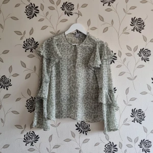 H&M grön blus, Strl: 34/XS - Fin grön blus med svarta prickar oxh vitt mönster från H&M med vida ärmar och volanger.