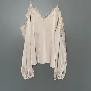 Beige satin blus i storlek L. Blusen är offshoulder med tunnare band över axlarna. Framtill finns mindre skador (se bild 3).