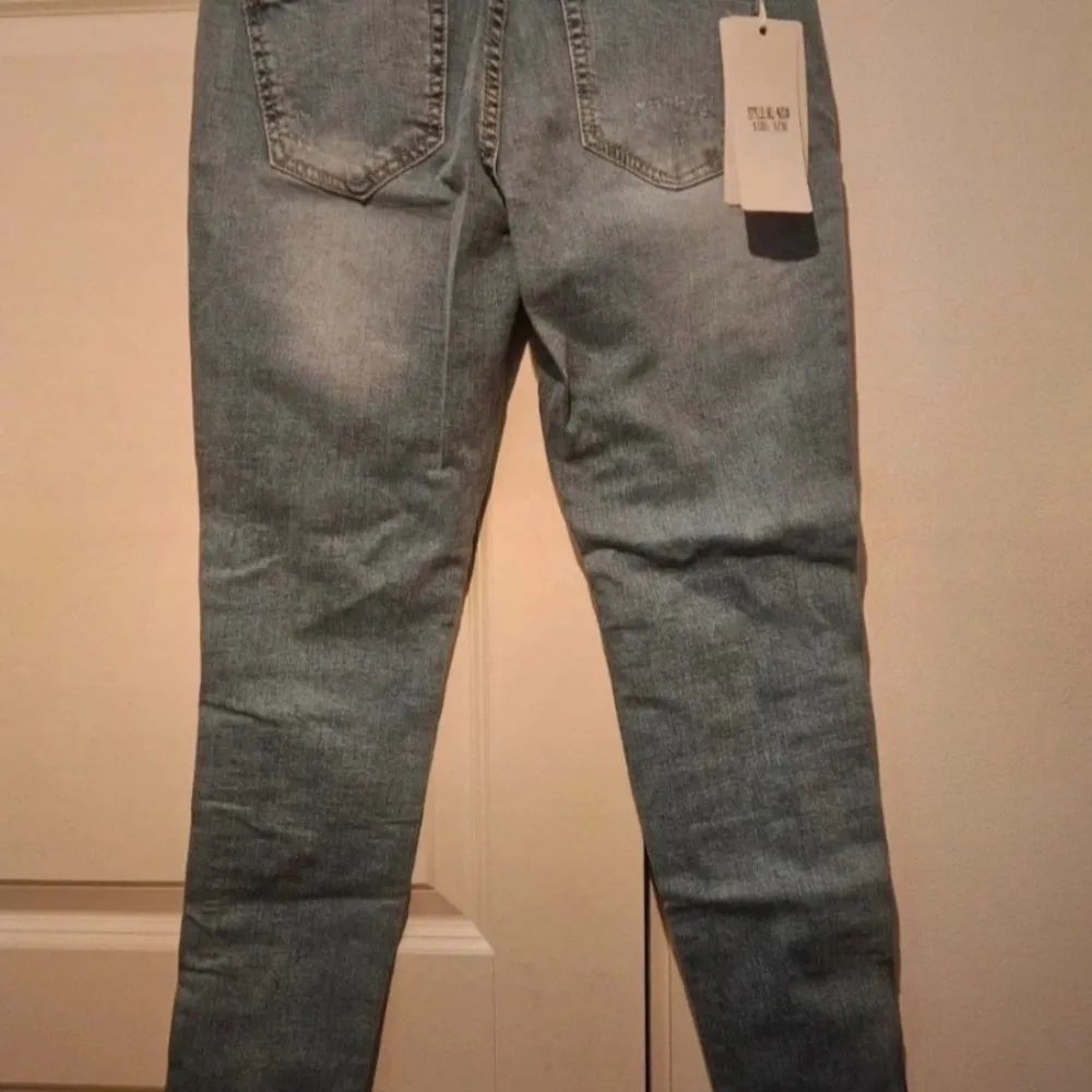 Helt nya jeans i ankle höjd. Fina slitningar och ett rött och vitt band längst sidan av benen. Kommer från ett djur och rökfritt hem . Jeans & Byxor.