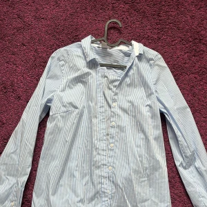 Randig skjorta - Blå och vitrandig skjorta från hm (dam). Knappar i ärmarna så att man kan vika upp. Veck framtill och baktill (utefter kroppsformen). Knapparna går inte ändå upp utan till brösthöjd. Perfekt till sommarn. Pris diskuterbart 👌🌞