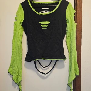 Ravetop - Beskrivning: Neongrön och svart top med alvärmar och öppen rygg.  Märke: Storlek: Medium Skick: Använd men i mycket gott skick, har ett litet hål på ena axeln, ca 7mm stort. Material: 100% bomull  Nakenkatt finns i hemmet