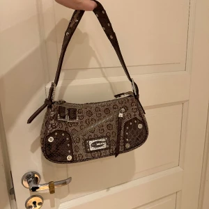 Guess väska - Guess väska köpt från usa ett par år tillbaka. Inga defekter förutom på drag kedjan där en liten bit av dragkedjan sticker ut från väskan och att den är lite trög att stänga annars är den i god kvalite.