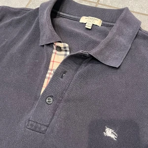 Burberry piké  - Säljer denna tvärfeta bueberry piké som är i bra skick och storlek L men passar M. Perfekt till sommaren! Nypris på dessa ligger på runt 5000kr! Tveka inte på att höra av er