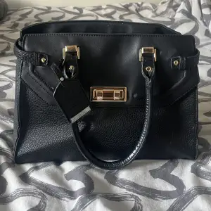 En svart väska med guld detajler, märket är okänt och väskan är använd men väldigt fint skick! 🫶🏼 