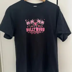 Svart t-shirt med snyggt rosa tryck som köptes second-hand. Varan är i bra skick och har inga defekter⭐️
