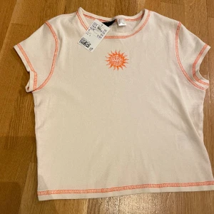 Vit t-shirt med orange detaljer  - Vit t-shirt med orange detaljer. Är helt oanvänd och har prislappen kvar. Säljer för att den är fel storlek för mig. 🧡
