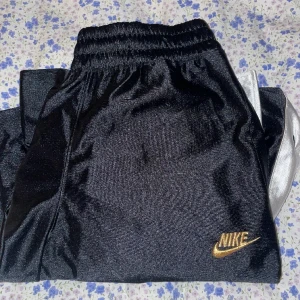 Nike byxor - Nike flared baggy byxor med vita ränder och knappar på sidorna. Knappt använt och inga defekter. Dm vid intresse/frågor!💕( Köpt på Nike för 899kr ) 