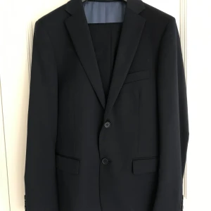 Mörkblå kostym med tillhörande byxor - Fin kostym med byxor i slim fit modell från dressman.  Använd fåtal gånger och är i nästintill nyskick. 