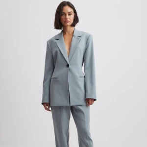 Blazer med knytning bak - Blazern är varken använd eller testad. Lappen är på och i förpackning!Jättesnygg! Köpte dock fel storlek så beställde i en annan storlek och älskar den❤️Färgen är grå med blåa undertoner. Modellen är 175cm lång och bär storlek 36 Nypris: 699kr